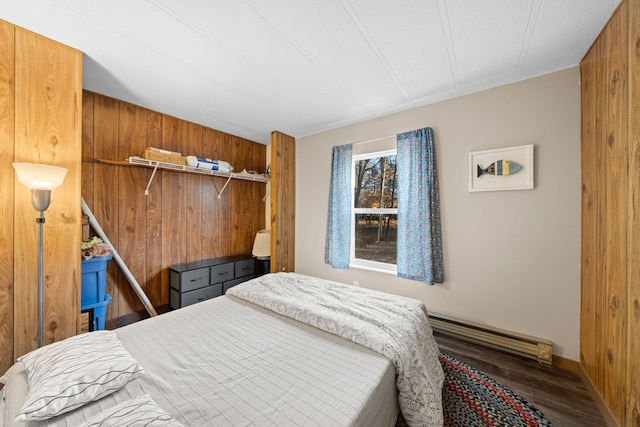 bedroom with a baseboard radiator, wood finished floors, and wood walls