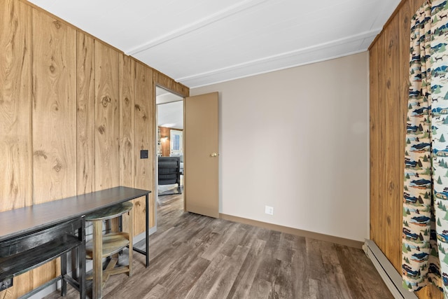 office space with a baseboard heating unit, wooden walls, wood finished floors, and baseboards
