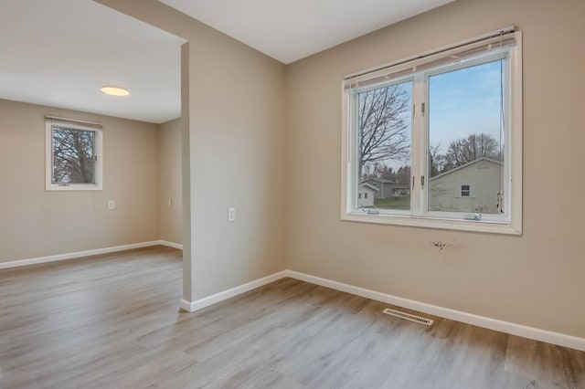 empty room featuring baseboards, a healthy amount of sunlight, wood finished floors, and visible vents