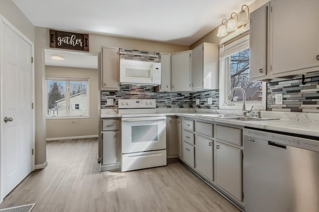 kitchen featuring a sink, white appliances, light wood-type flooring, light countertops, and backsplash