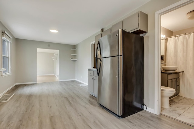 kitchen featuring a sink, light wood finished floors, baseboards, visible vents, and freestanding refrigerator