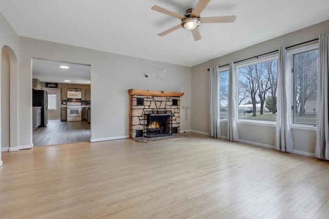living area with a ceiling fan, arched walkways, light wood finished floors, a fireplace, and baseboards