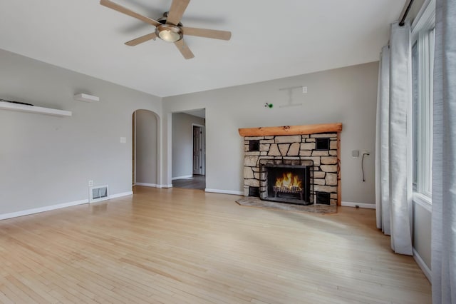 unfurnished living room with wood finished floors, visible vents, arched walkways, and ceiling fan