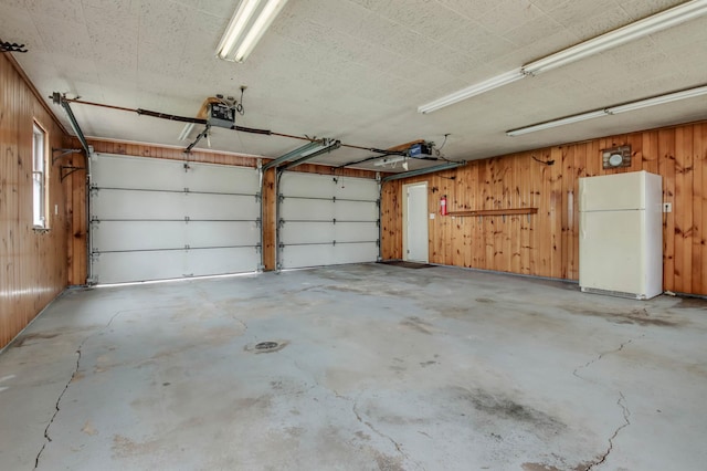 garage featuring a garage door opener, wooden walls, and freestanding refrigerator