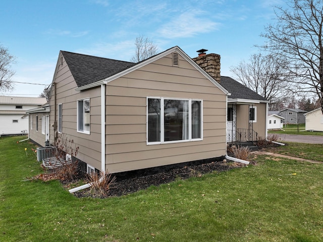 view of side of home featuring a lawn, a chimney, and roof with shingles