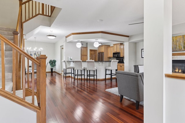 living area with dark wood-style flooring, a fireplace, a notable chandelier, and stairway
