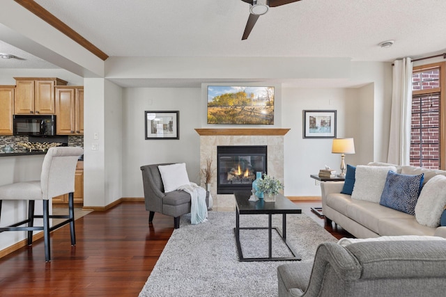 living area with a ceiling fan, baseboards, dark wood-style floors, and a tiled fireplace