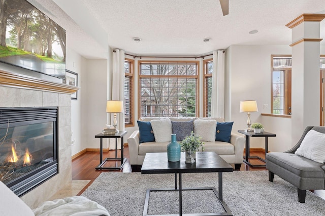 living room featuring baseboards, a textured ceiling, wood finished floors, and a tile fireplace
