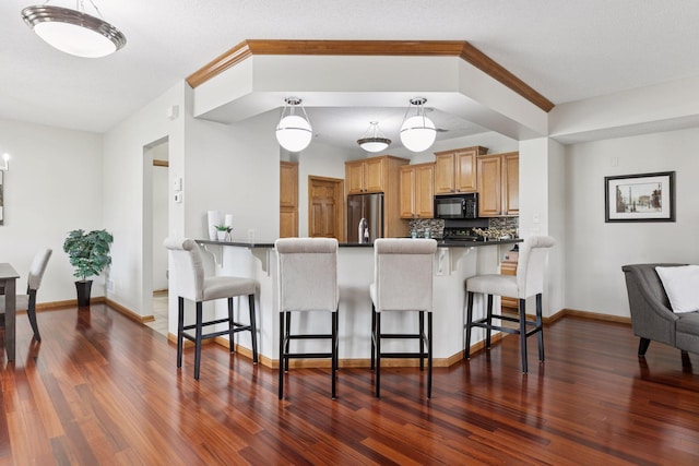 kitchen featuring a breakfast bar area, dark countertops, black microwave, and stainless steel refrigerator
