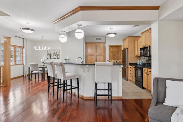 kitchen with wood finished floors, dark countertops, a kitchen breakfast bar, a sink, and black appliances