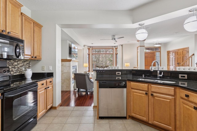 kitchen with tasteful backsplash, a sink, light tile patterned floors, black appliances, and a premium fireplace