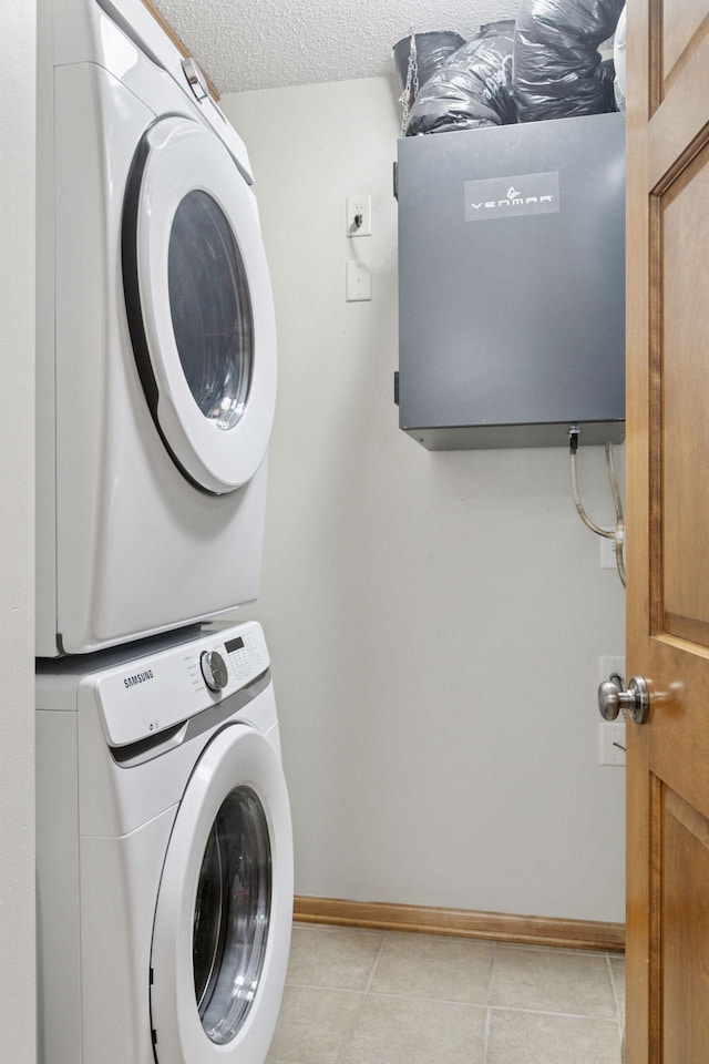 clothes washing area featuring laundry area, stacked washer and clothes dryer, light tile patterned flooring, baseboards, and a textured ceiling