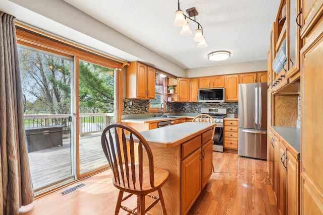 kitchen featuring appliances with stainless steel finishes, a sink, a center island, backsplash, and visible vents
