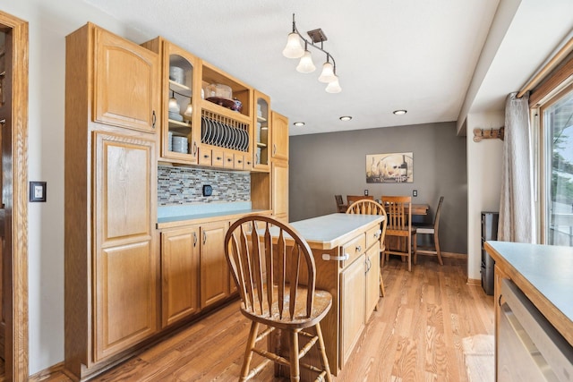 kitchen with tasteful backsplash, light wood finished floors, light countertops, a kitchen bar, and glass insert cabinets