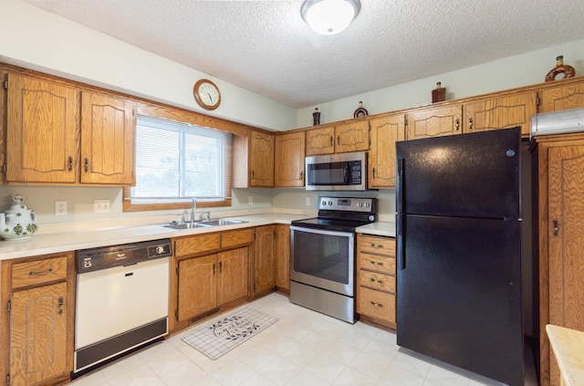 kitchen with appliances with stainless steel finishes, a sink, a textured ceiling, brown cabinets, and light countertops