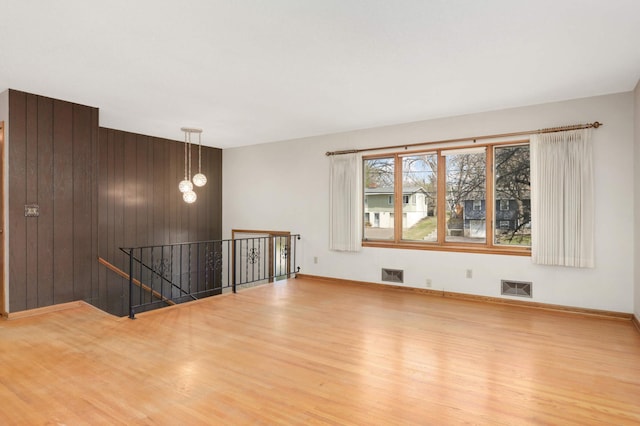 spare room featuring a chandelier, wood walls, wood finished floors, and visible vents