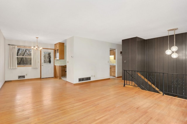 unfurnished living room with an inviting chandelier, light wood-style flooring, and visible vents