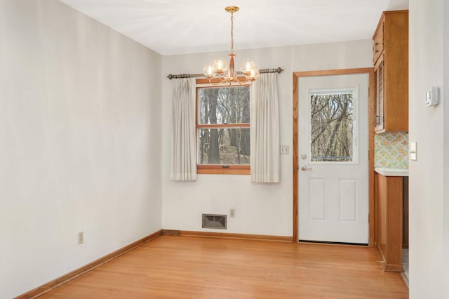 unfurnished dining area featuring light wood-style floors, a healthy amount of sunlight, visible vents, and a chandelier