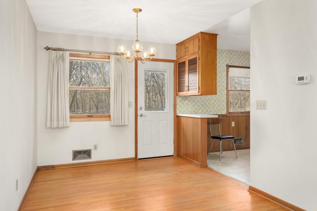 unfurnished dining area featuring light wood-style floors, baseboards, a notable chandelier, and visible vents