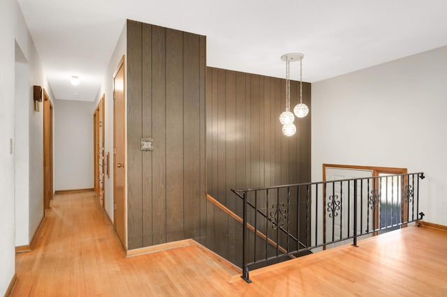 hallway with baseboards, wood finished floors, wooden walls, and an upstairs landing