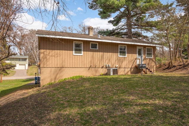 exterior space with a shingled roof, entry steps, a chimney, cooling unit, and a yard