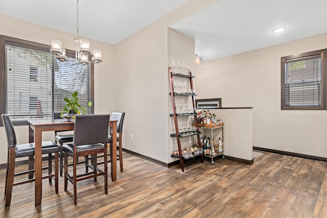 dining area with baseboards, a bar, wood finished floors, and a notable chandelier
