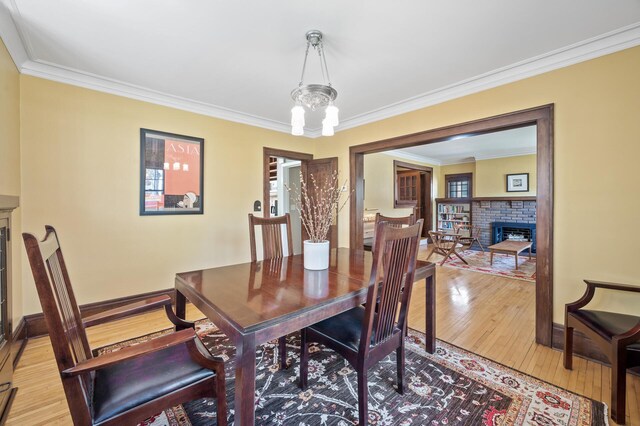 dining room with crown molding, a notable chandelier, light wood-style floors, a fireplace, and baseboards