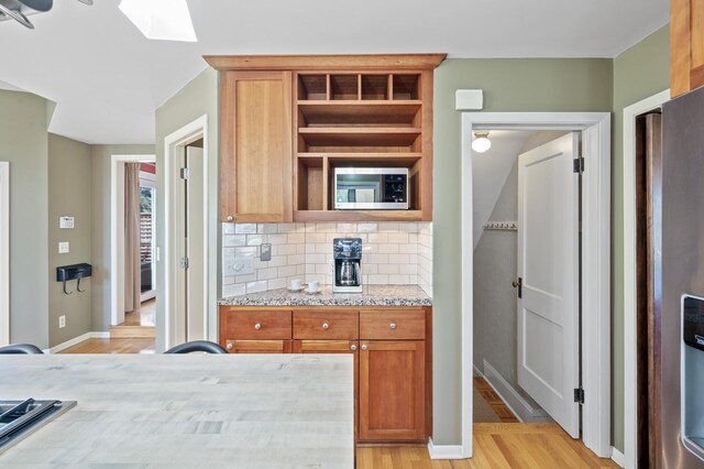 kitchen featuring a skylight, tasteful backsplash, open shelves, stainless steel microwave, and light wood finished floors