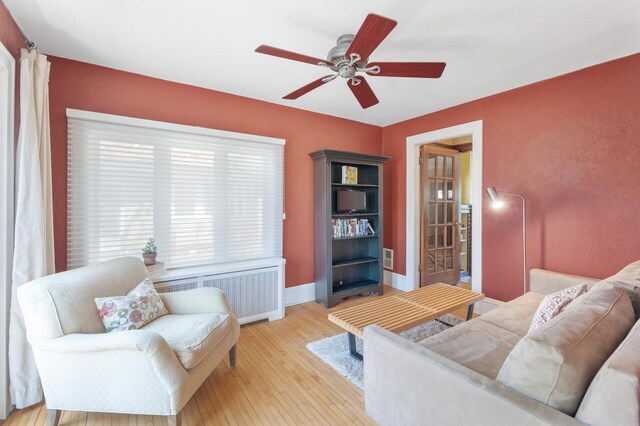 living area with light wood-type flooring, a ceiling fan, radiator, and baseboards