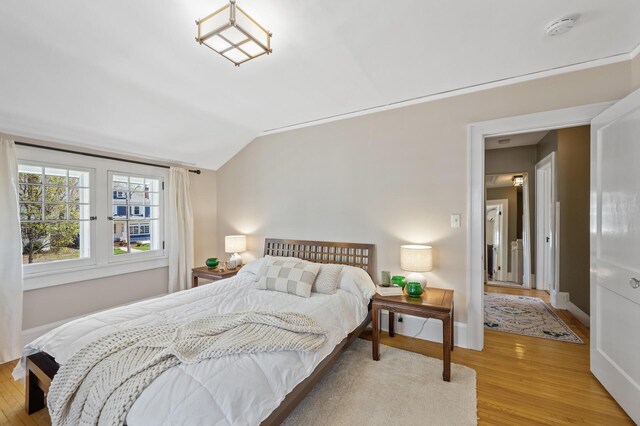 bedroom featuring baseboards, vaulted ceiling, and light wood-type flooring