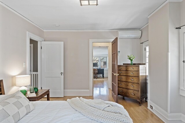 bedroom with wood finished floors, baseboards, crown molding, and a wall mounted AC