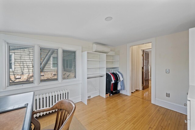 office space featuring baseboards, a wall unit AC, light wood finished floors, and radiator