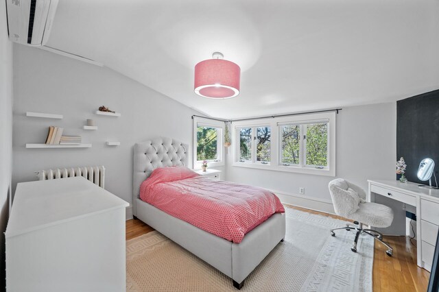 bedroom featuring light wood-type flooring, radiator heating unit, and vaulted ceiling