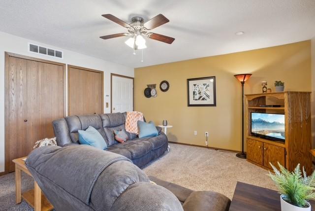 living area with baseboards, a ceiling fan, visible vents, and light colored carpet