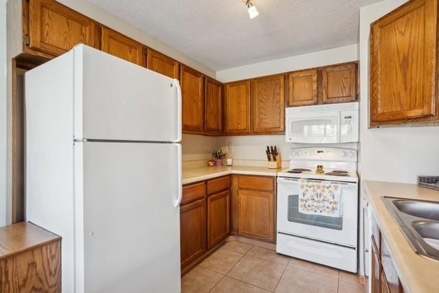 kitchen with brown cabinets, a sink, white appliances, and light countertops