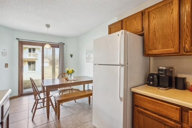 kitchen with light countertops, freestanding refrigerator, decorative light fixtures, brown cabinetry, and a textured ceiling