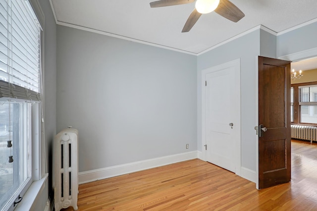 spare room with light wood-style floors, radiator heating unit, crown molding, and ceiling fan with notable chandelier
