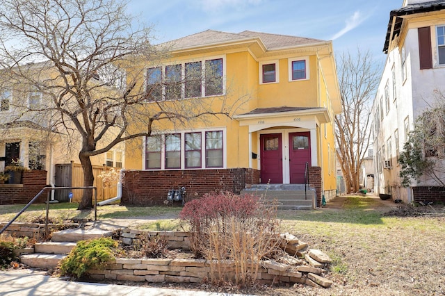 view of front of house featuring stucco siding, fence, a shingled roof, and brick siding