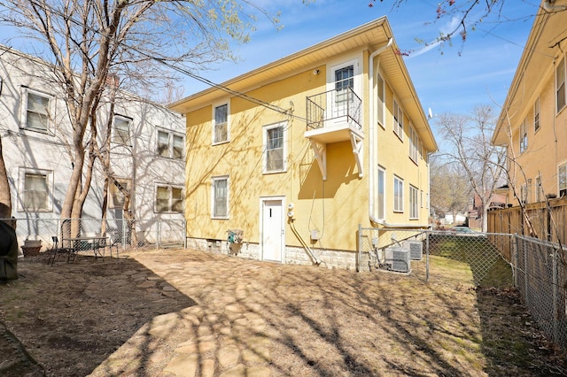 rear view of property featuring a fenced backyard, a balcony, central air condition unit, and stucco siding