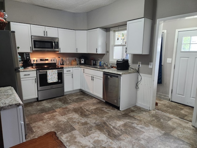 kitchen with appliances with stainless steel finishes, a sink, stone finish flooring, and white cabinets