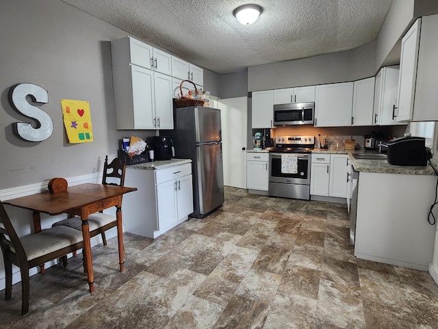 kitchen with stainless steel appliances, a textured ceiling, white cabinets, stone finish floors, and a sink