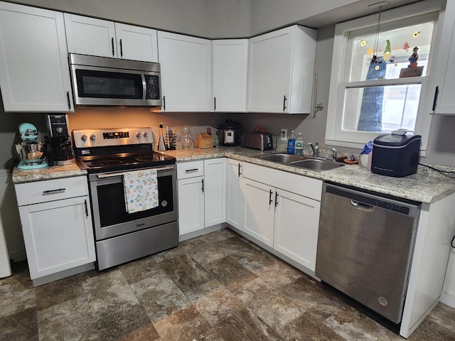 kitchen featuring stainless steel appliances, a sink, stone finish floors, and white cabinets