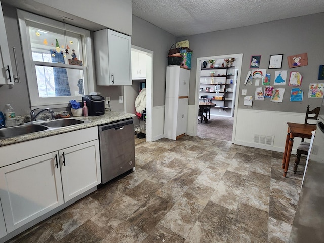 kitchen featuring stainless steel dishwasher, a sink, a textured ceiling, white cabinets, and light stone finish flooring