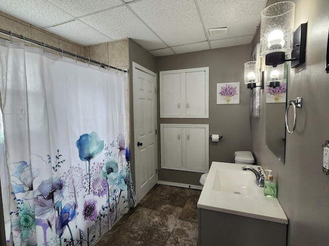 bathroom with a drop ceiling, toilet, vanity, a shower with shower curtain, and stone finish floors