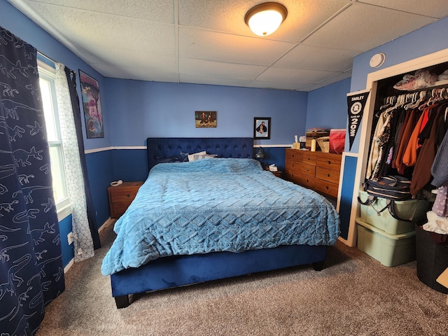 carpeted bedroom featuring a drop ceiling, multiple windows, and a closet