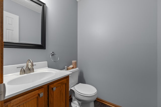 half bath featuring wood finished floors, vanity, and toilet