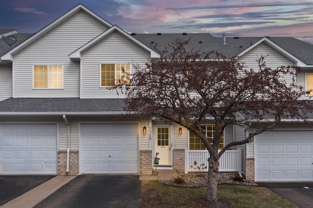 view of front of house featuring an attached garage, driveway, roof with shingles, and brick siding