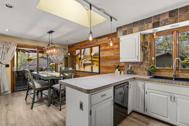1302 Birch Dr, Hudson, WI 54016 - kitchen featuring dishwasher, a sink, healthy amount of natural light, wood walls, and white cabinets
