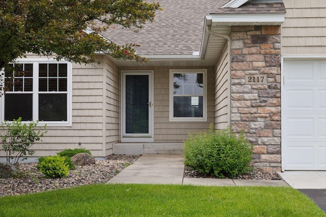 2117 14th St NE, Faribault, MN 55021 - doorway to property with roof with shingles, stone siding, and a garage
