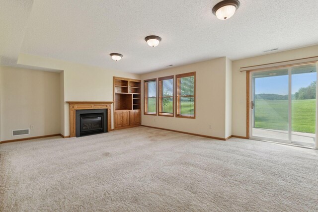 2117 14th St NE, Faribault, MN 55021 - unfurnished living room with a textured ceiling, healthy amount of natural light, a glass covered fireplace, light colored carpet, and built in shelves